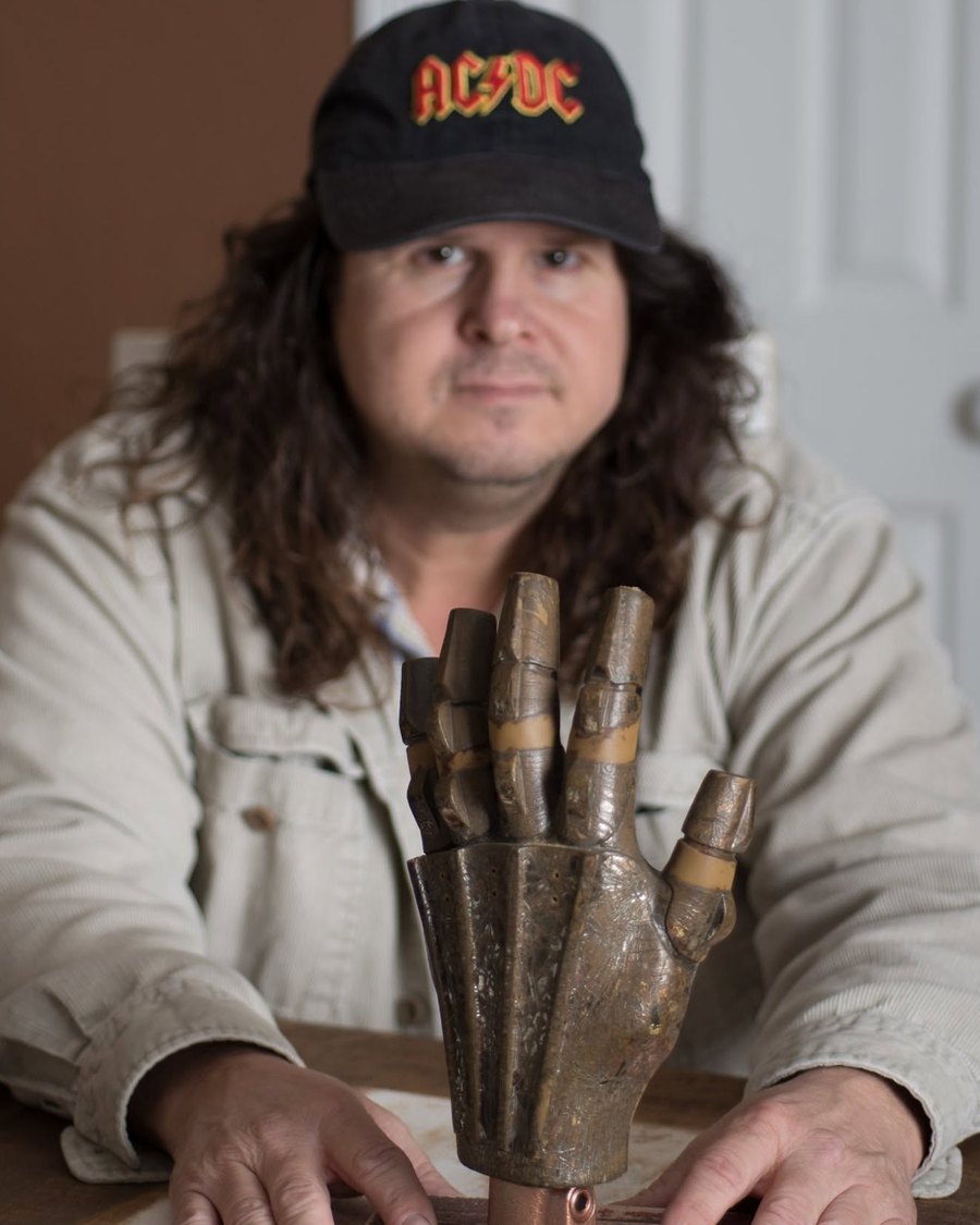 Jeff Castillo, founder of Icons of Pop Culture, seated behind a metal robotic hand prop